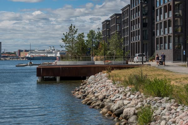 Kajpromenad med brygga och bostadshus längs kajen. 